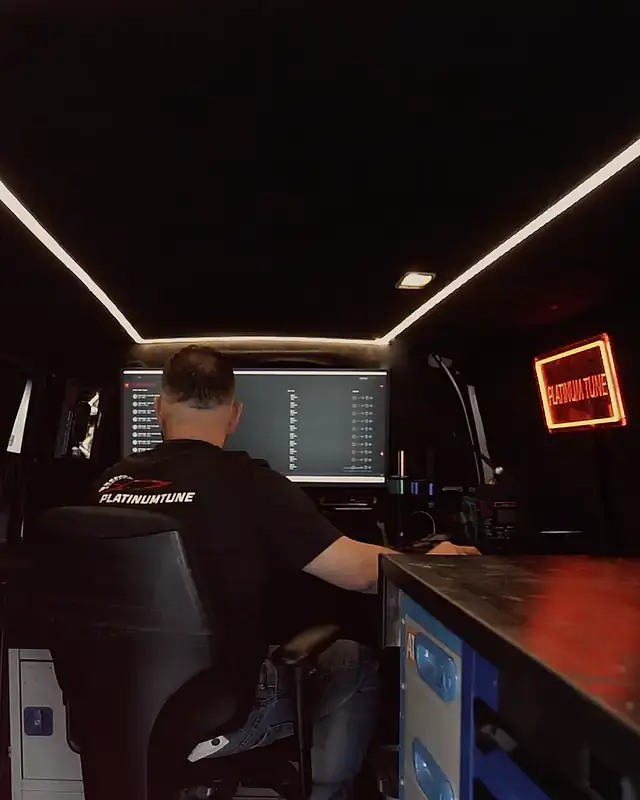 Mobile remapping: a tuner at the bench under the LED ceiling, the red Platinum Tune neon sign on the wall
