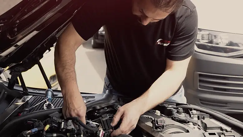 A Platinum Tune technician with his hands on the engine harness of a customer's car, bonnet up