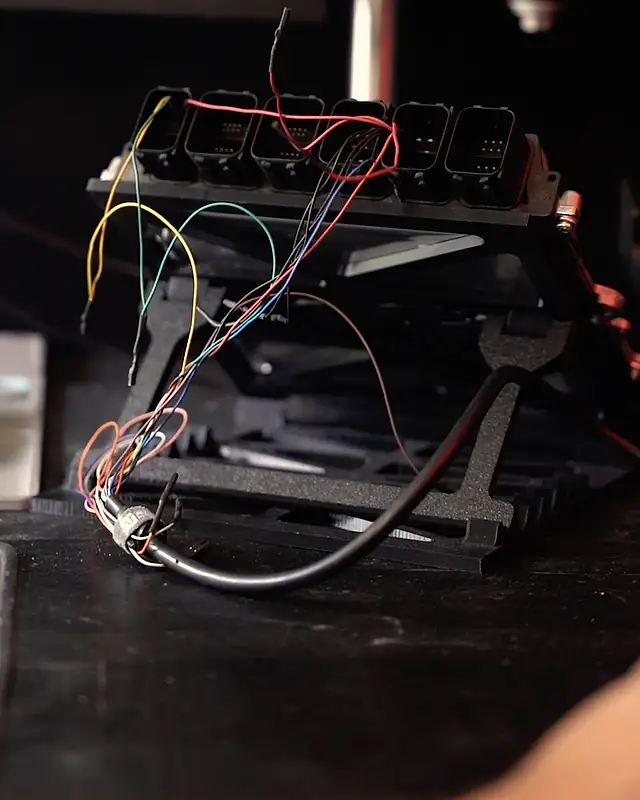 An ECU on the bench frame with coloured jumper wires, ready for a read